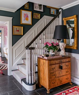 A hallway with black painted walls, walnut chest, white painted woodwork and art on the walls