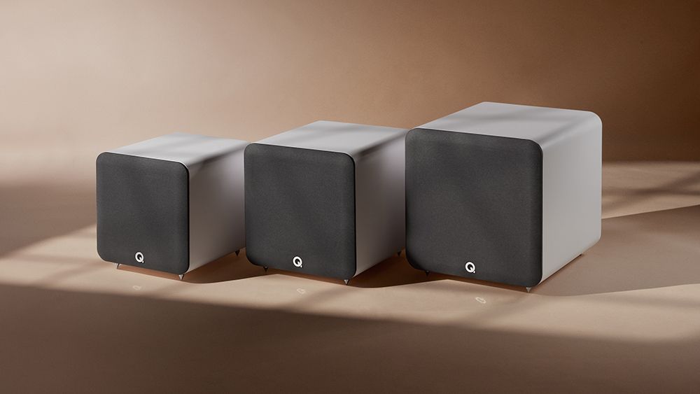 Q Acoustics&#039; three Q SUB models side by side against a brown backdrop