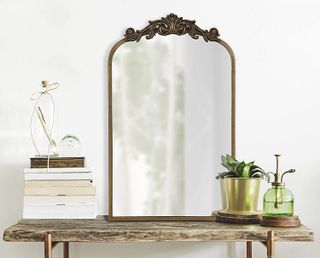 arched ornate brass mirror standing on a shelf with books and other decor
