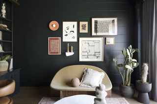 A small living room painted charcoal black, juxtaposed with neutral artworks on the wall and a biscuit-toned sofa