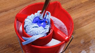 A mop being wrung in a red bucket after mopping a hardwood floor