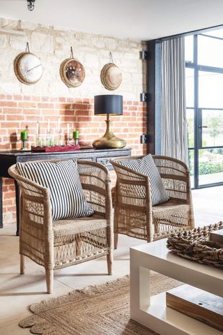 Two wicker chairs in a foyer with an exposed brick feature wall