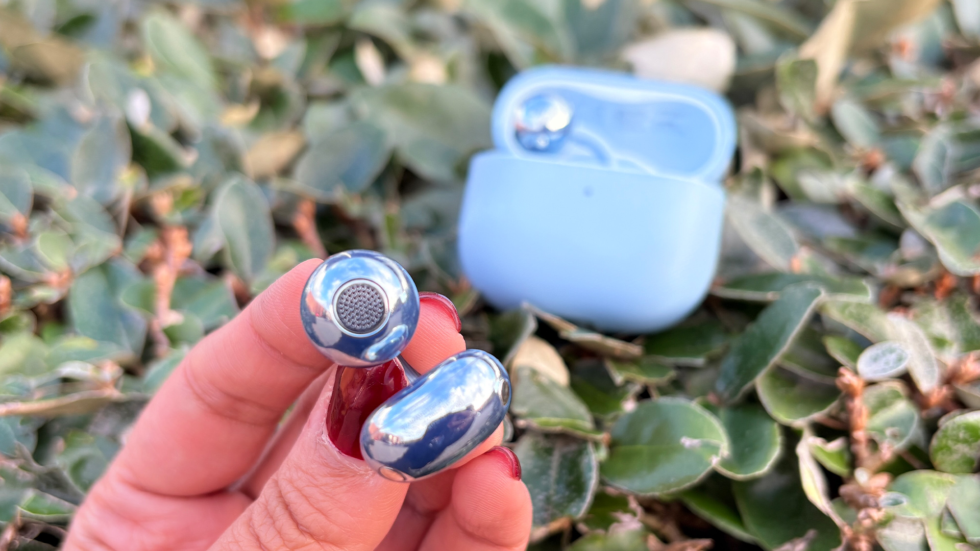 Huawei FreeClip 2 wireless earbuds one bud held in hand, case nestled in bush