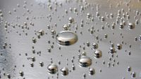 A series of silver circular droplets shine against a silvery metal surface