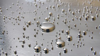 A series of silver circular droplets shine against a silvery metal surface