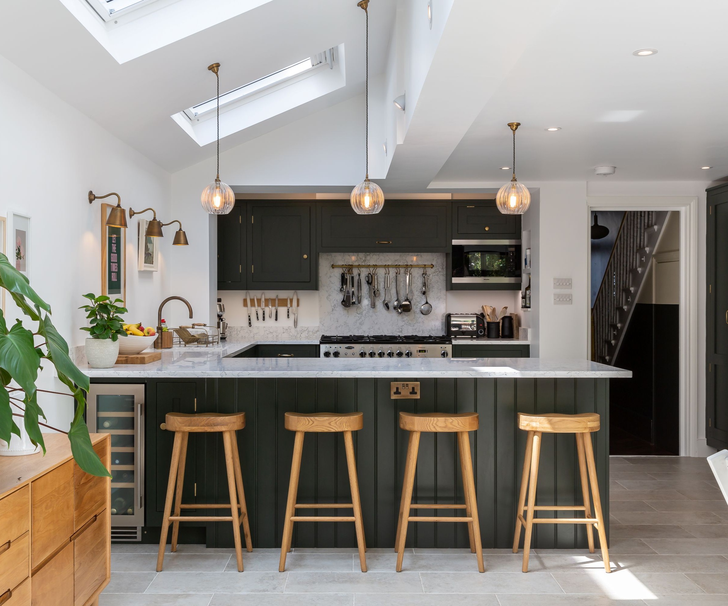 A kitchen with deep green kitchen cabinets and four wooden stools at an island