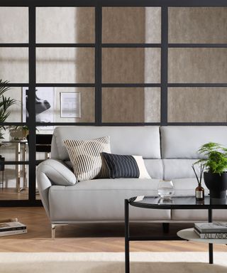 A grey leather sofa in a living room with black-framed Crittal-style glass and cream cushions
