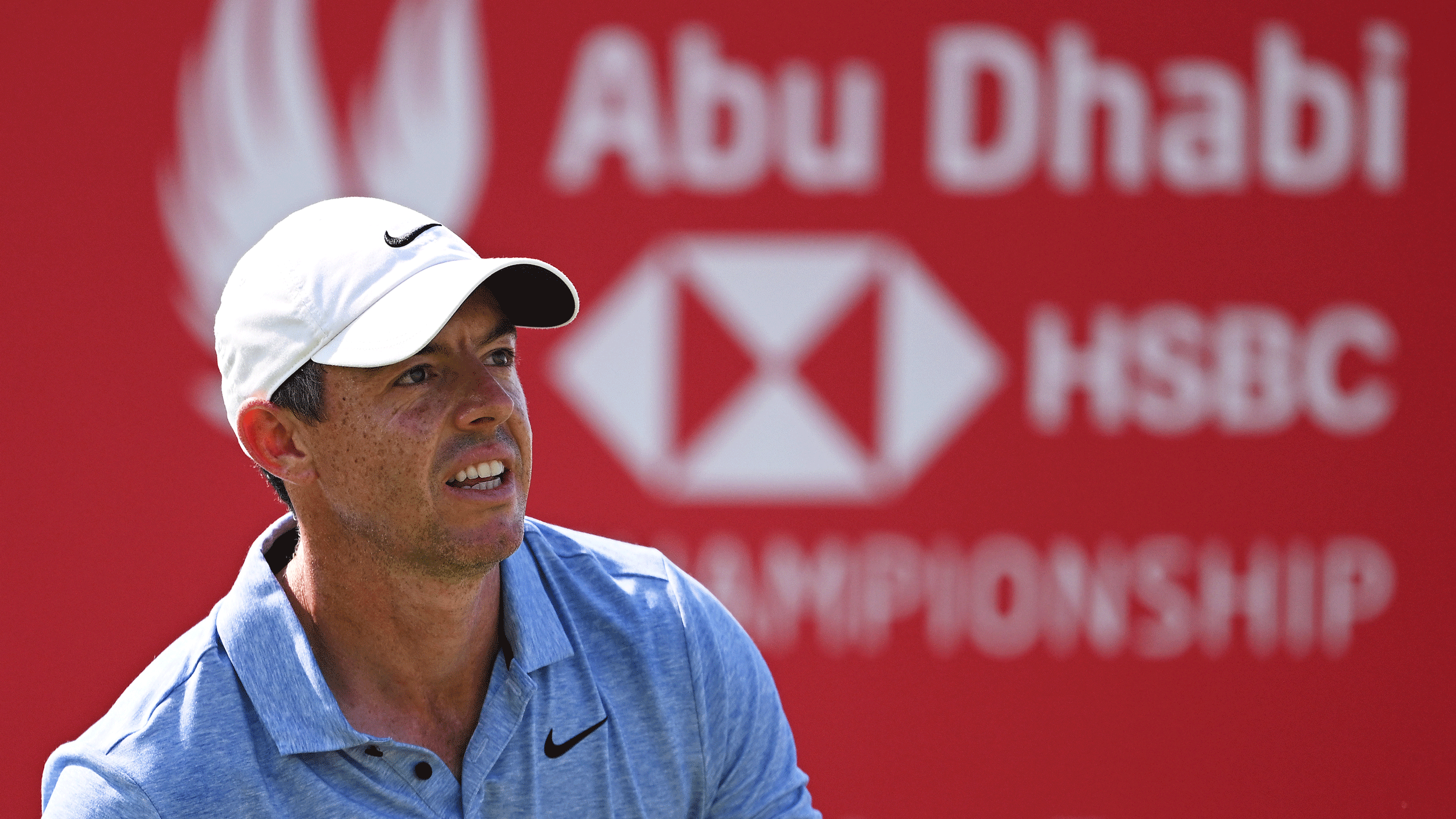 Rory McIlroy looks on with the Abu Dhabi HSBC Championship sign blurred slightly in the background