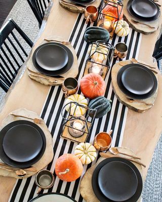 Pale wood table with balck and white striped runner and pumpkins