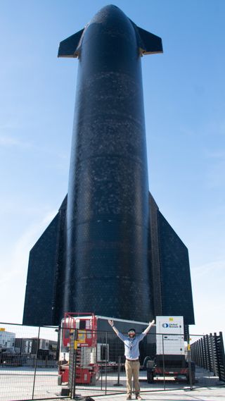 a bearded man stands in front of a rocket
