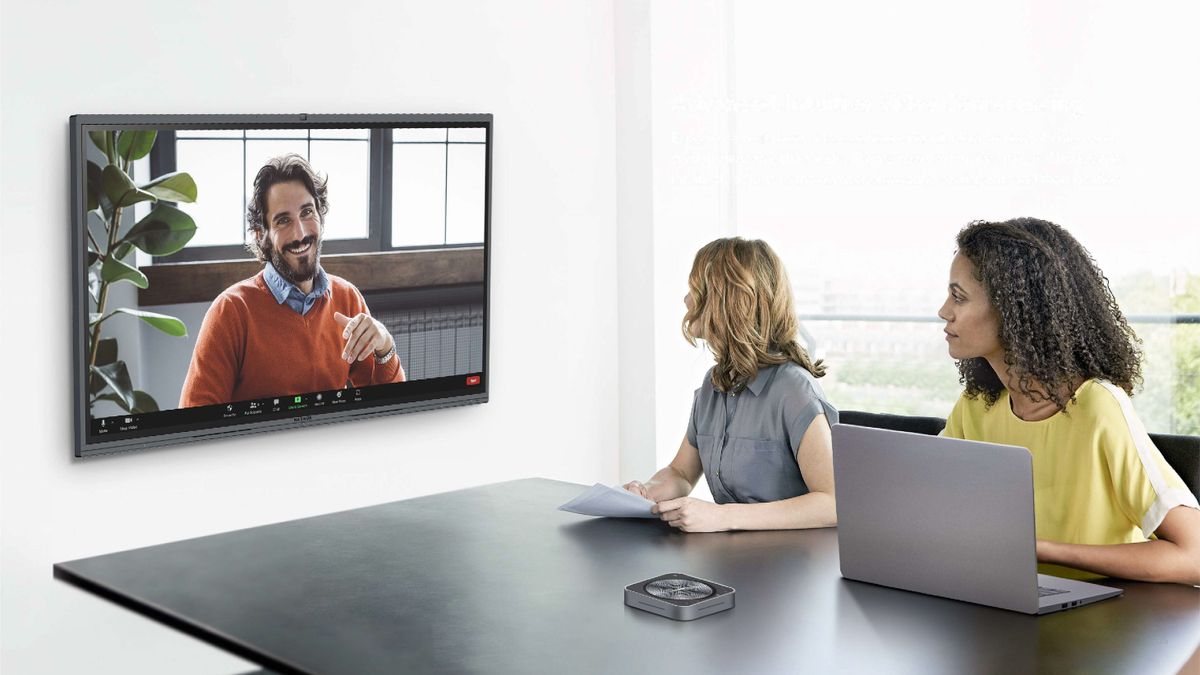 Two women in a conference room speaking to a smiling man on the new MAXHUB flat panel.