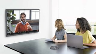 Two women in a conference room speaking to a smiling man on the new MAXHUB flat panel.
