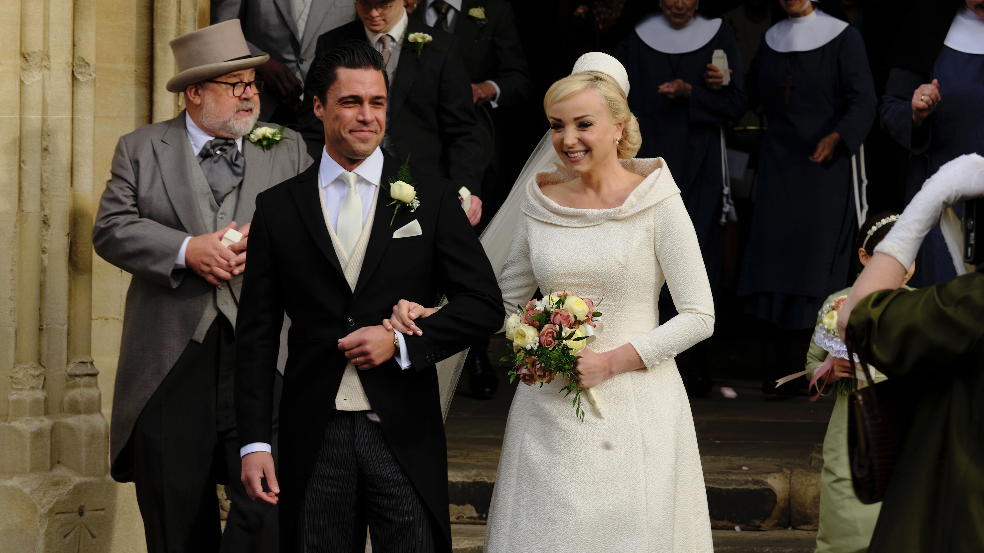 Olly Rix and Helen George as Matthew and Trixie in wedding clothes stand outside a church in Call the Midwife
