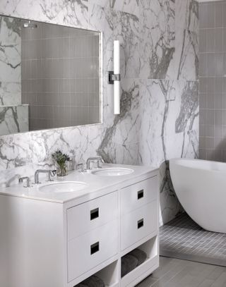 marble tiled bathroom with white vanity, white tub, double sink