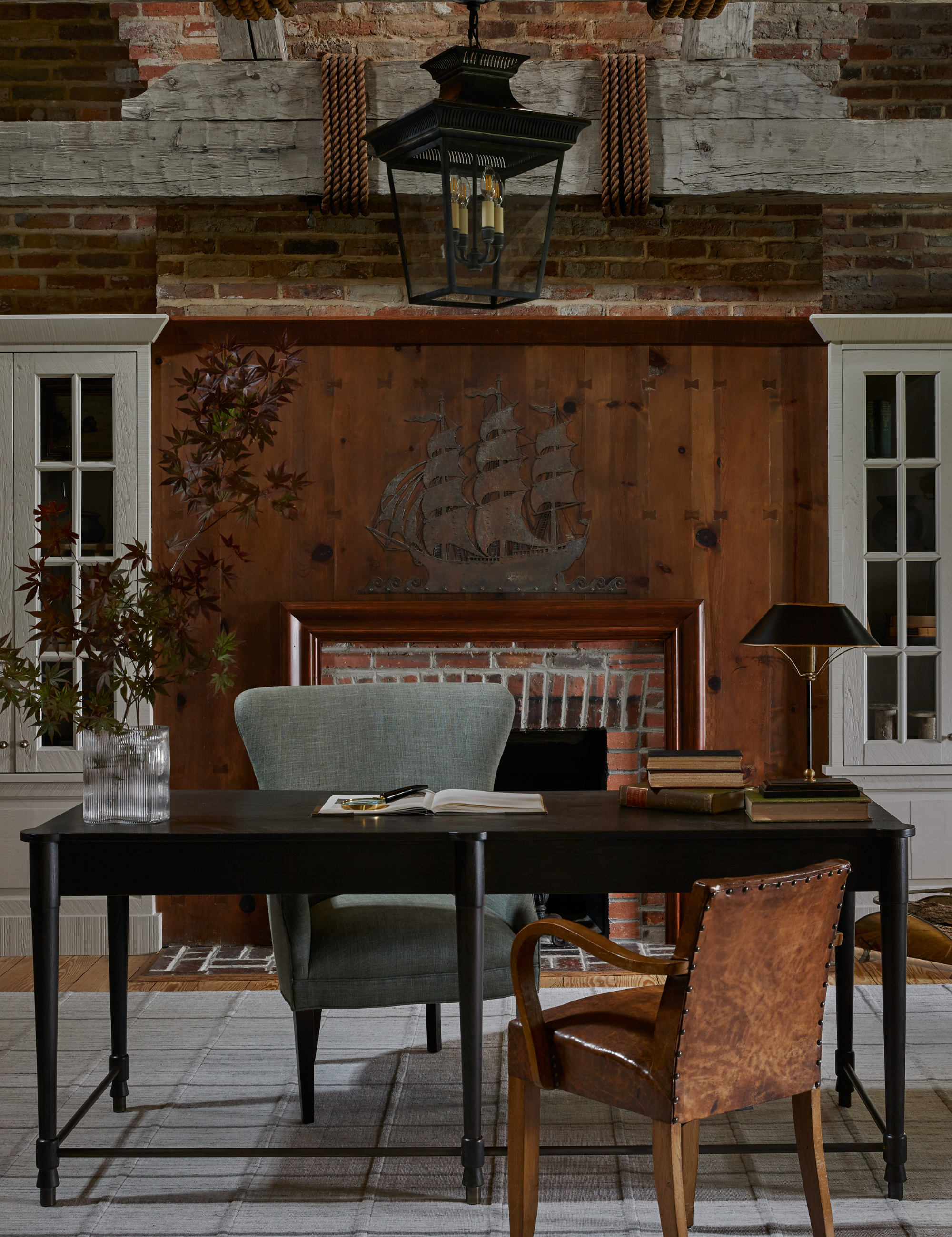 Nautical office area with exposed brick, dark walnut wood, and a metal ship motif hanging above the wooden mantle.