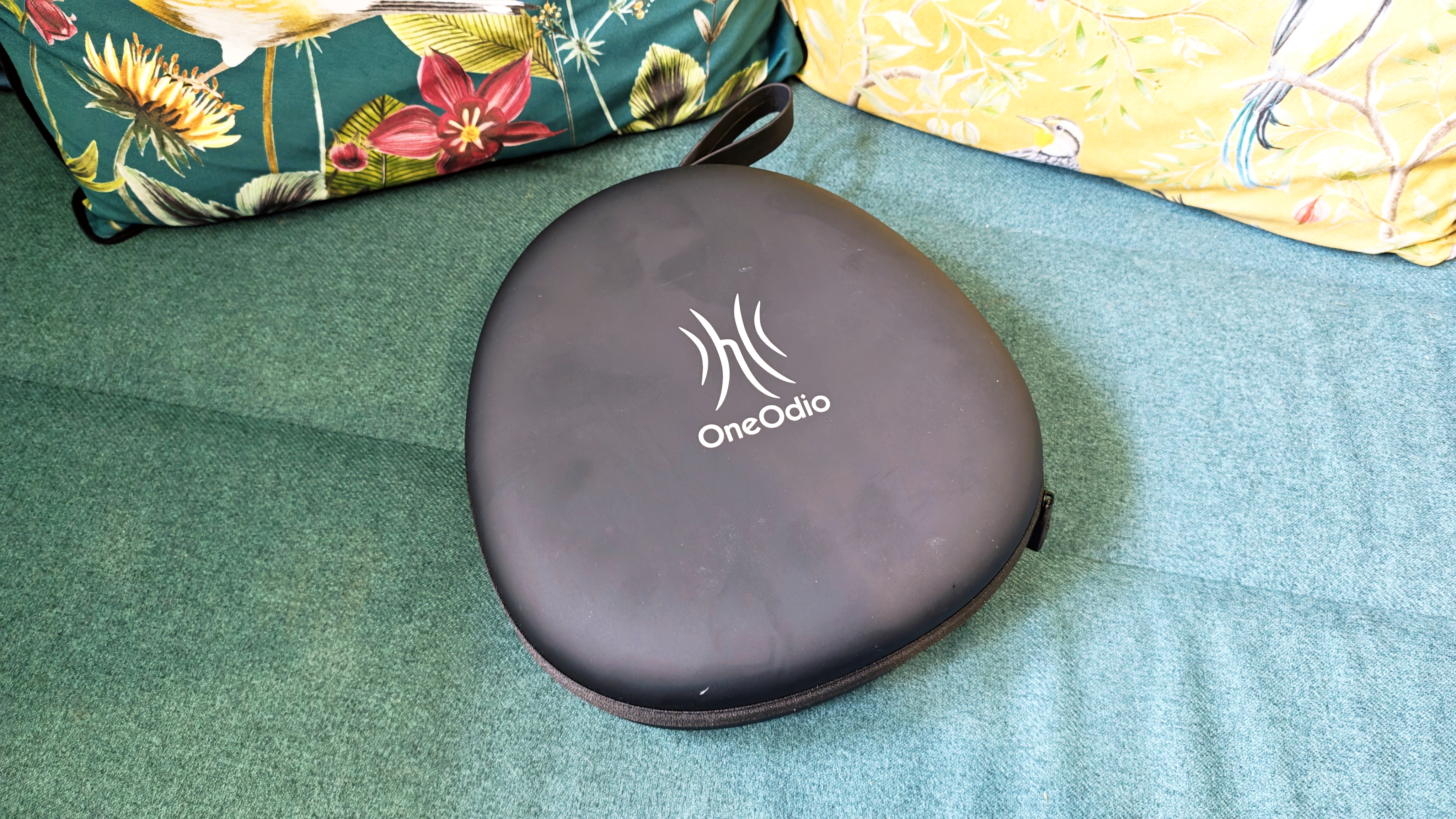 A pair of black OneOdio Studio Max 2 headphones with red internal earcups sitting on a green sofa in front of colourful pillows with birds and flowers on them