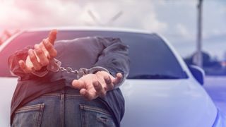 Handcuffed person face-down on the hood of a police car