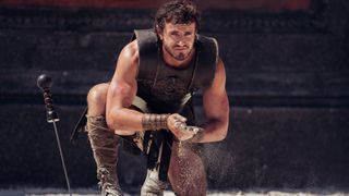 A still from Paramount Pictures' Gladiator 2 with Paul Mescal kneeling in an arena with sand running through his fingers.