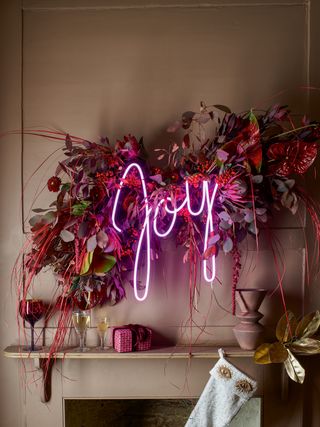 Neon Joy sign in a dried flower garland hung above a fireplace