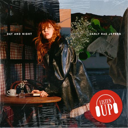 Carly Rae Jepsen poses in a long leather trench coat leaning over a table with a collage behind her on the cover of her album day and night 
