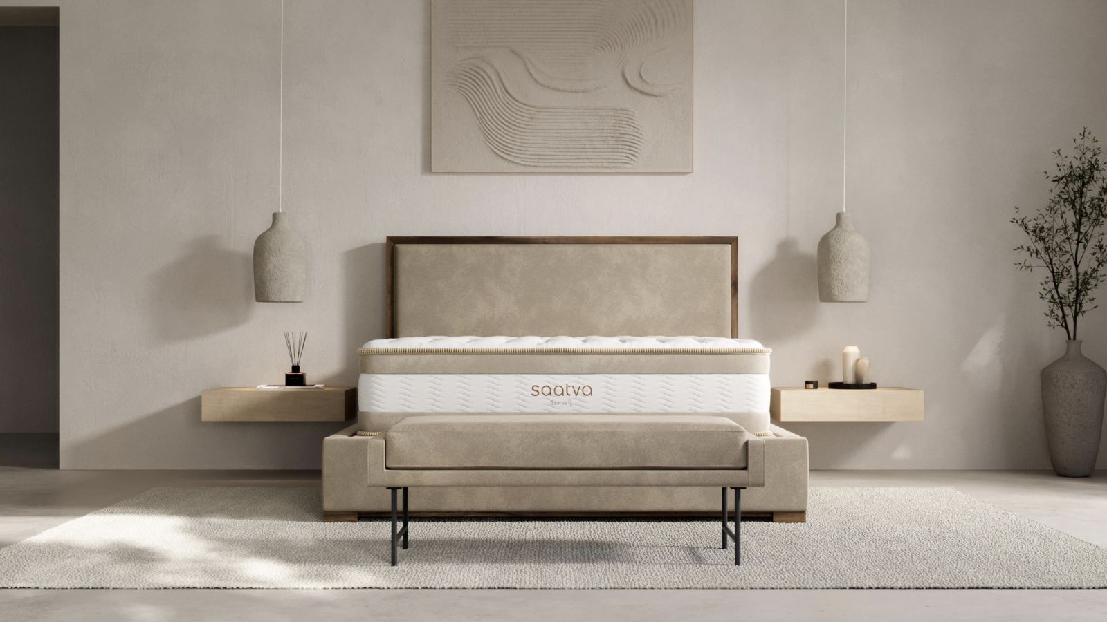 A Saatva Rx mattress in a minimalist cream bedroom on a beige bedframe, with a white rug underneath, and two wooden bedside tables to either side. Above the nightstands are two ceramic hanging lamps, and above the bed is a large grey artwork. To the right is a large grey pot with a tree growing.