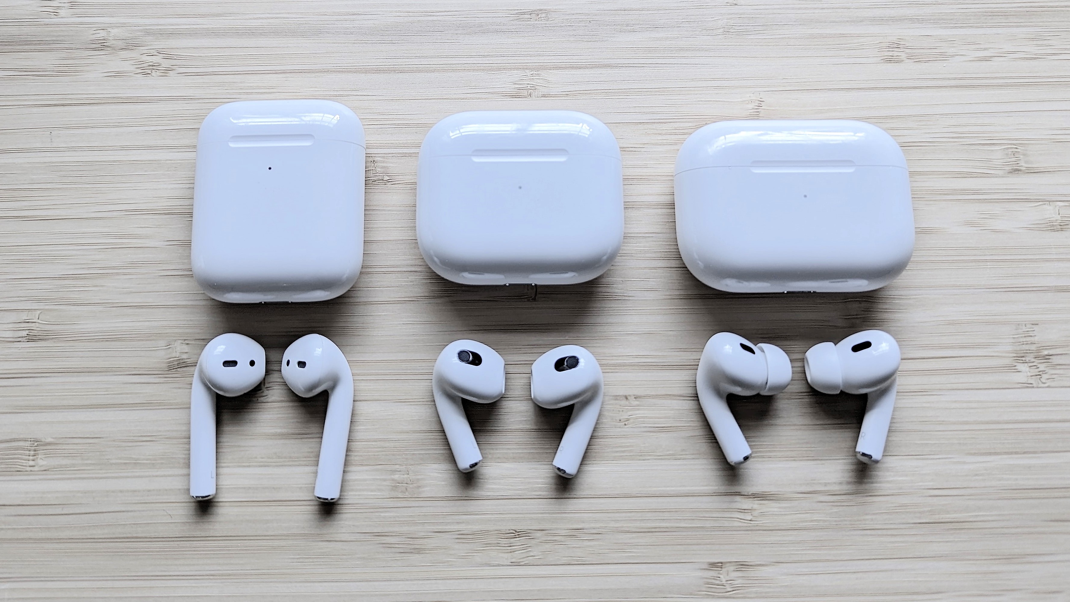 3 AirPods with charging cases lined up on a wooden surface