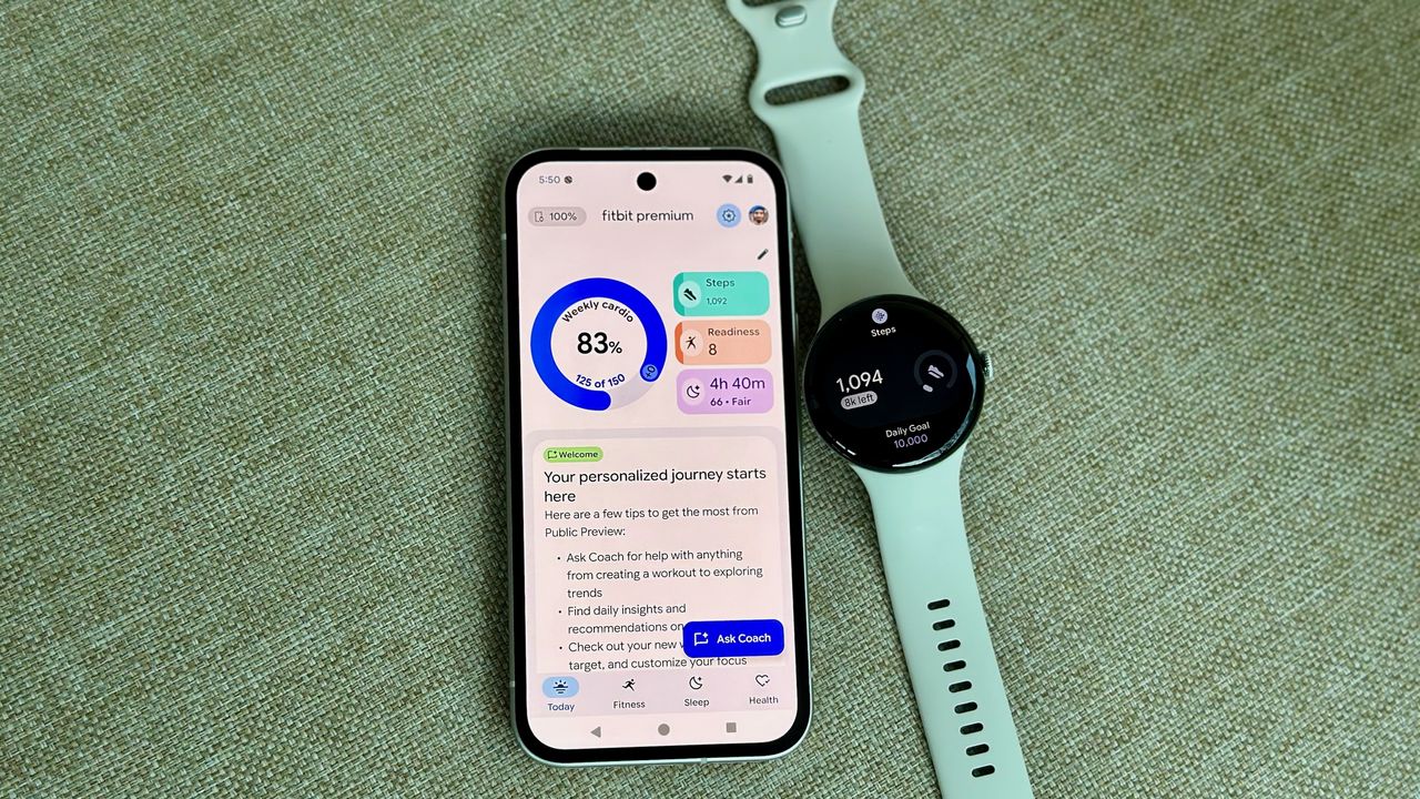 A photo of the Google Pixel Watch 4 sitting next to a Pixel 9a open to the Fitbit app, showing the Fitbit Premium Health Coach preview with the Today tab open; it shows new widgets and insights.