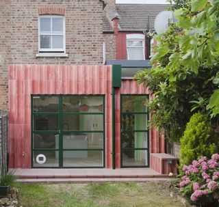 a rear extension in red concrete with green doors