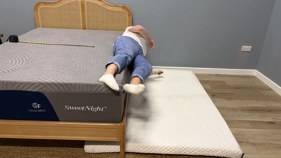 A tester rests right on the edge of the SweetNight CoolNest Mattress. A thin mattress is positioned on the floor next to the bed, to cushion her if she should fall off the bed.