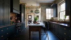 A Victorian home's kitchen with dark green cabinets, a freestanding island, copper countertops, and handpainted mottled paint walls