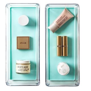 Two clear storage trays on a white background with a selection of beauty products stored in them