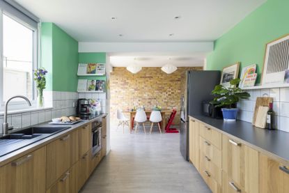 bright open plan wooden kitchen diner, with green feature walls and a brick effect wall