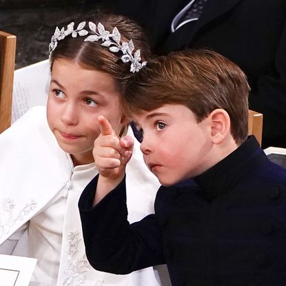 Princess Charlotte wears a white cape and has a leafy silver crown, while Prince Louis wears a navy coat and points