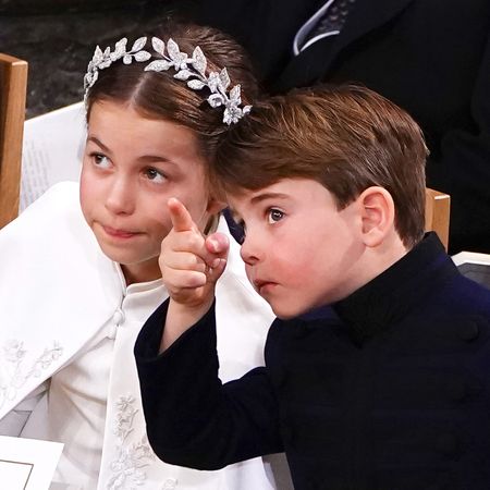 Princess Charlotte wears a white cape and has a leafy silver crown, while Prince Louis wears a navy coat and points