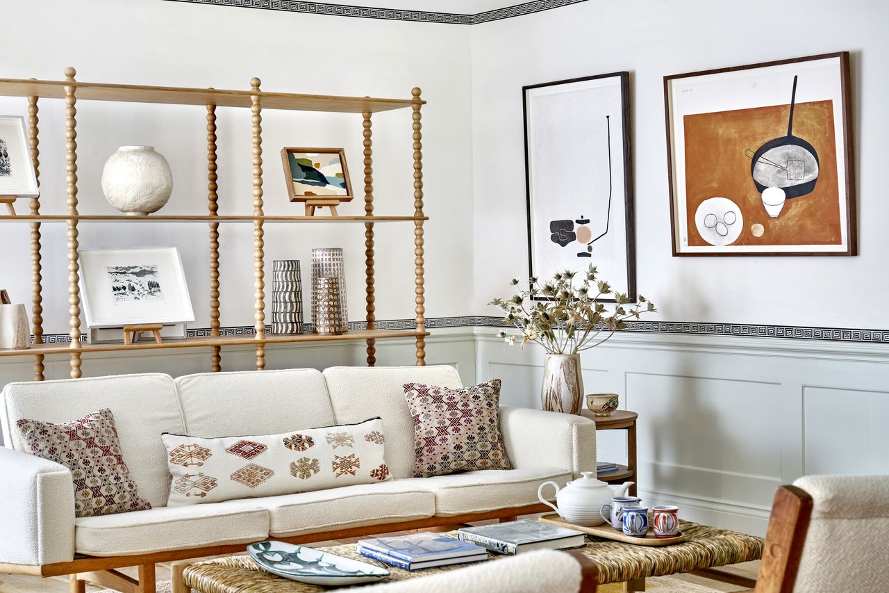 A living room with neutral decor and a black and white Grecian wallpaper border above the wall panelling 