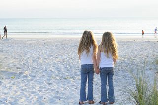 Twin girls standing on the beach holding hands.