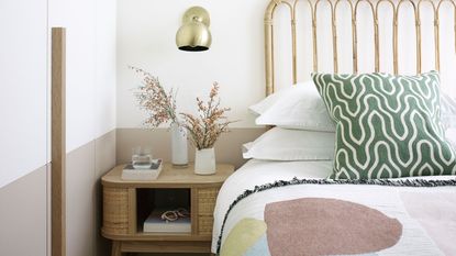 bed with rattan headboard, gold wall sconce and a wooden side table 