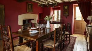 wooden table and chairs in a red walled dining room with beams on the ceiling