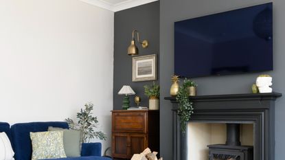 A living room with a dark grey feature wall with a TV above a wood burning stove surrounded by a fireplace mantel