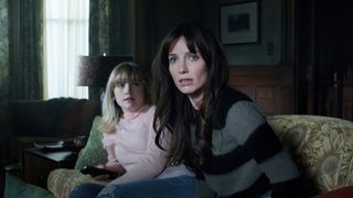 A still from the movie Malignant in which main character Madison Mitchell is sat in a living room with a little girl and looks scared.