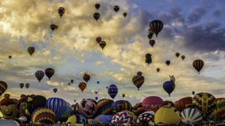 hundreds of hot air balloons fill the sky and take off from the ground.