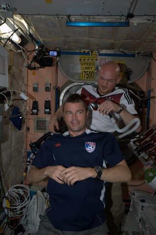 One astronaut shaves another astronaut's head in microgravity on the international space station