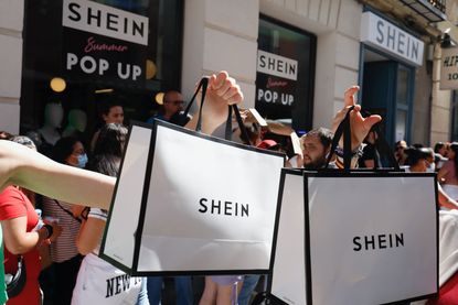 People holding white Shein shopping bags outside of Shein store popup in Madrid