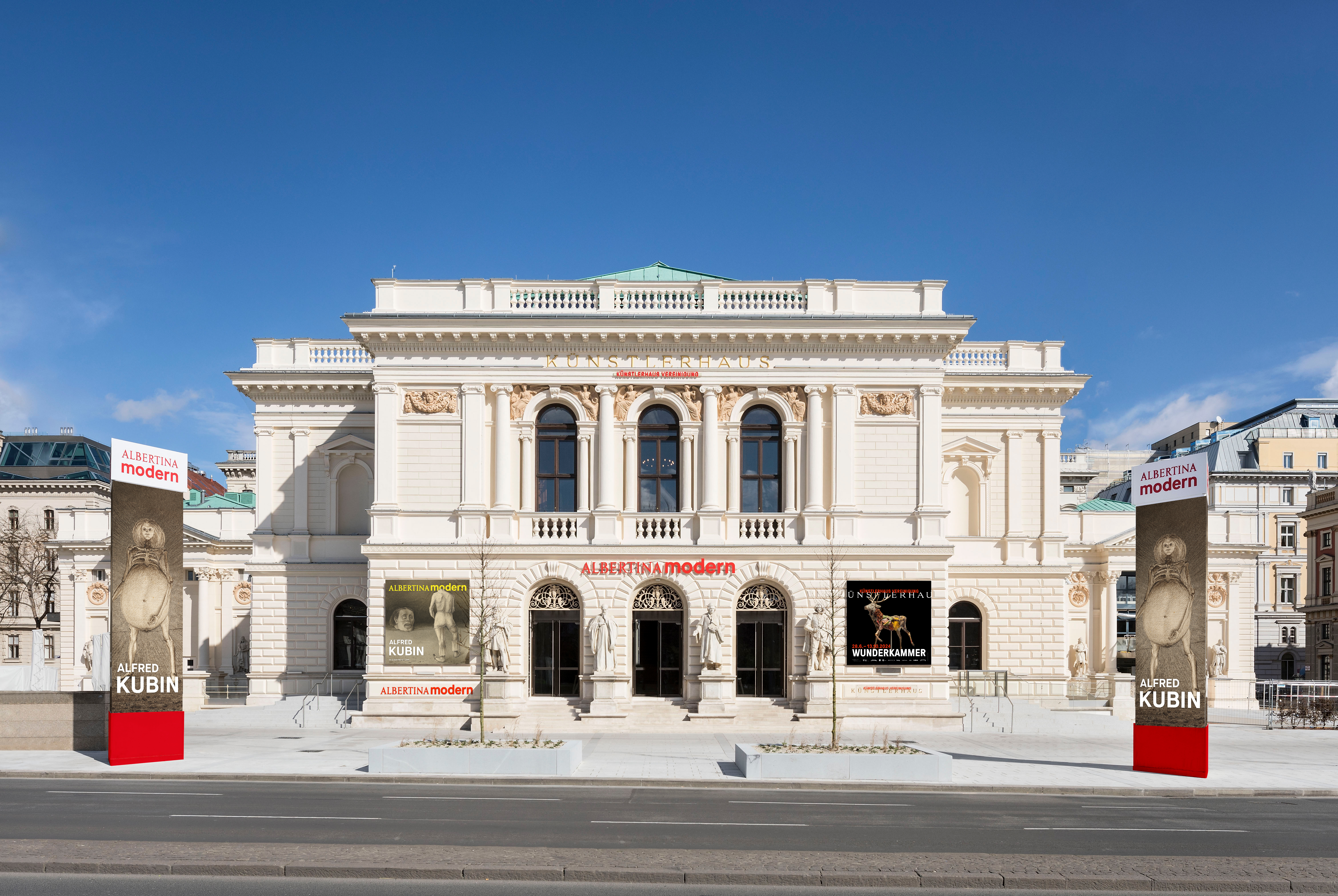 An historical building with a stuccoed white, light brown, and light green facade and the sign &quot;Albertina Modern&quot; in red is illuminated by a sunny day.