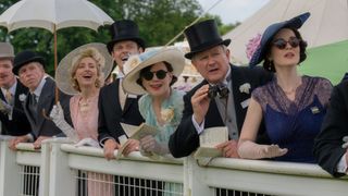 The Crawley family at the races in their fancy clothes and watching horses come towards them which are off screen