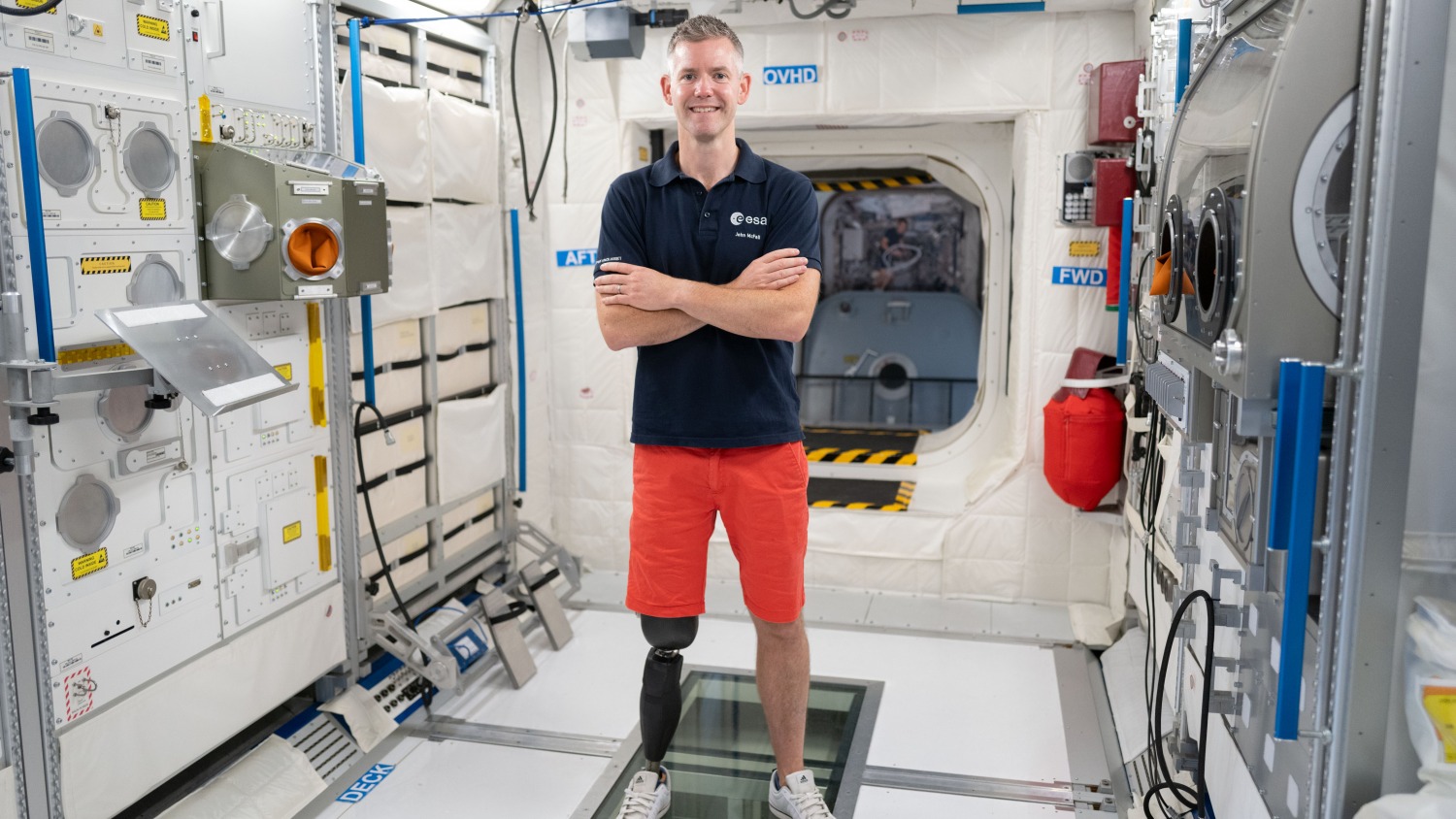 An astronaut stands in an ISS module with a prosthesis on his right leg