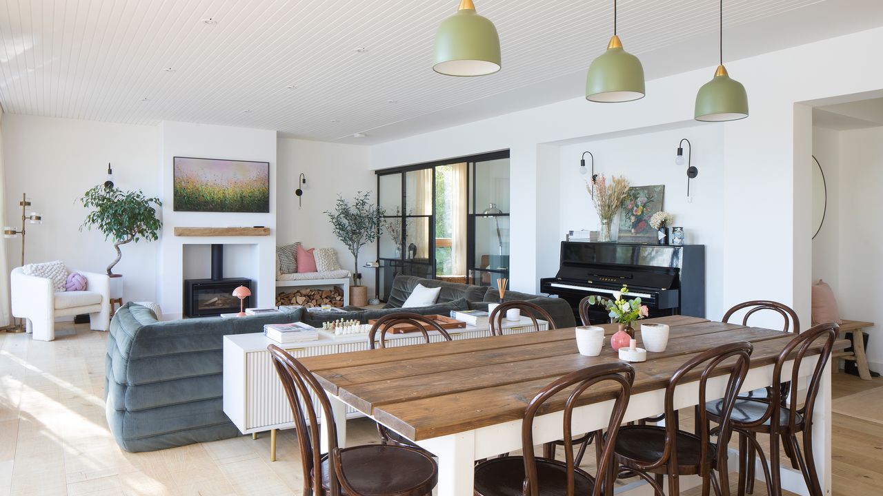 A modern open-plan living room, dining area and kitchen with slubby low sofa, woodburning stove and wooden dining set