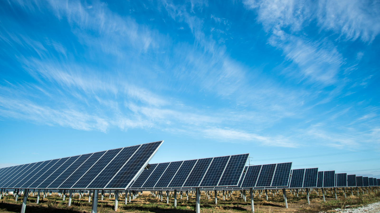 A series of solar panel rows in a field under a blue sky with wisps of clouds.