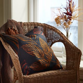fall decor cushion on rattan chair with dried flowers in a vase in fall colors
