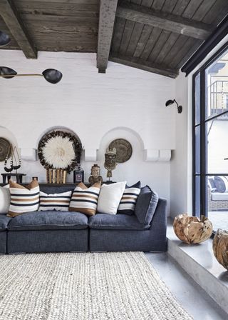 garden room with wooden beamed paneled ceiling white arched walls and big glass windows with grey sofa and striped cushions